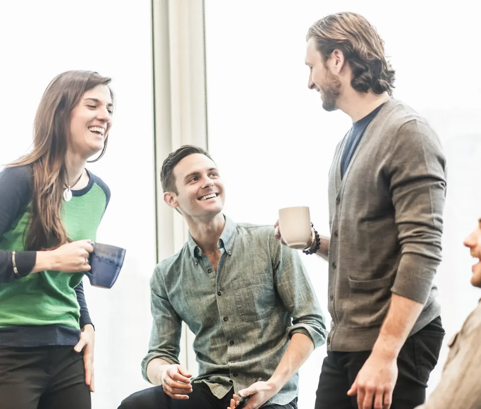 Vier collega’s lachen samen tijdens een pauze in een licht kantoor