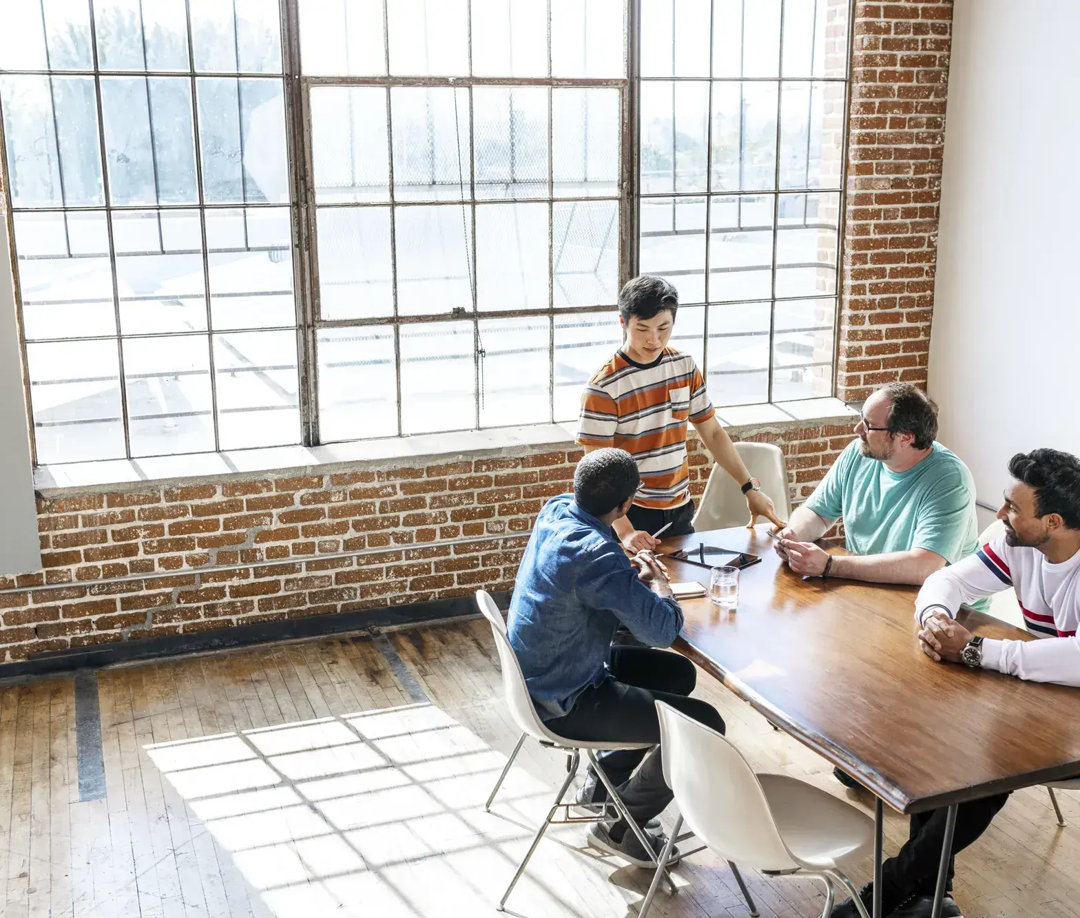 Team overlegt aan een lange tafel in een loft met een groot raam