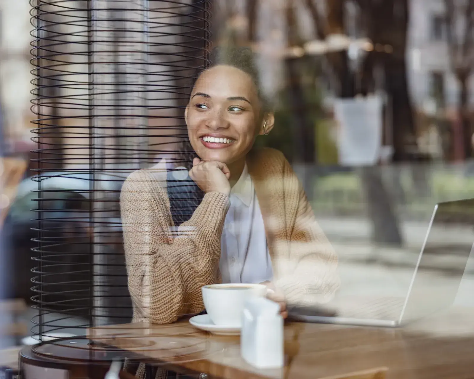 HR-professional zit lachend achter haar laptop bij het raam, met een kop koffie