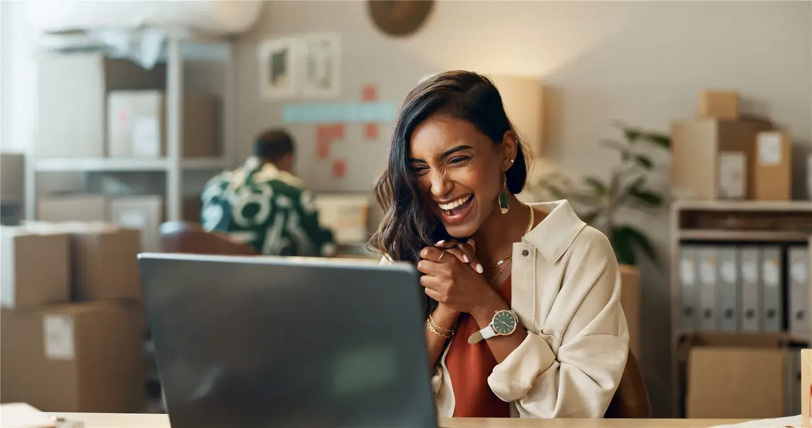 HR-medewerker werkt lachend achter haar laptop in een warm kantoor