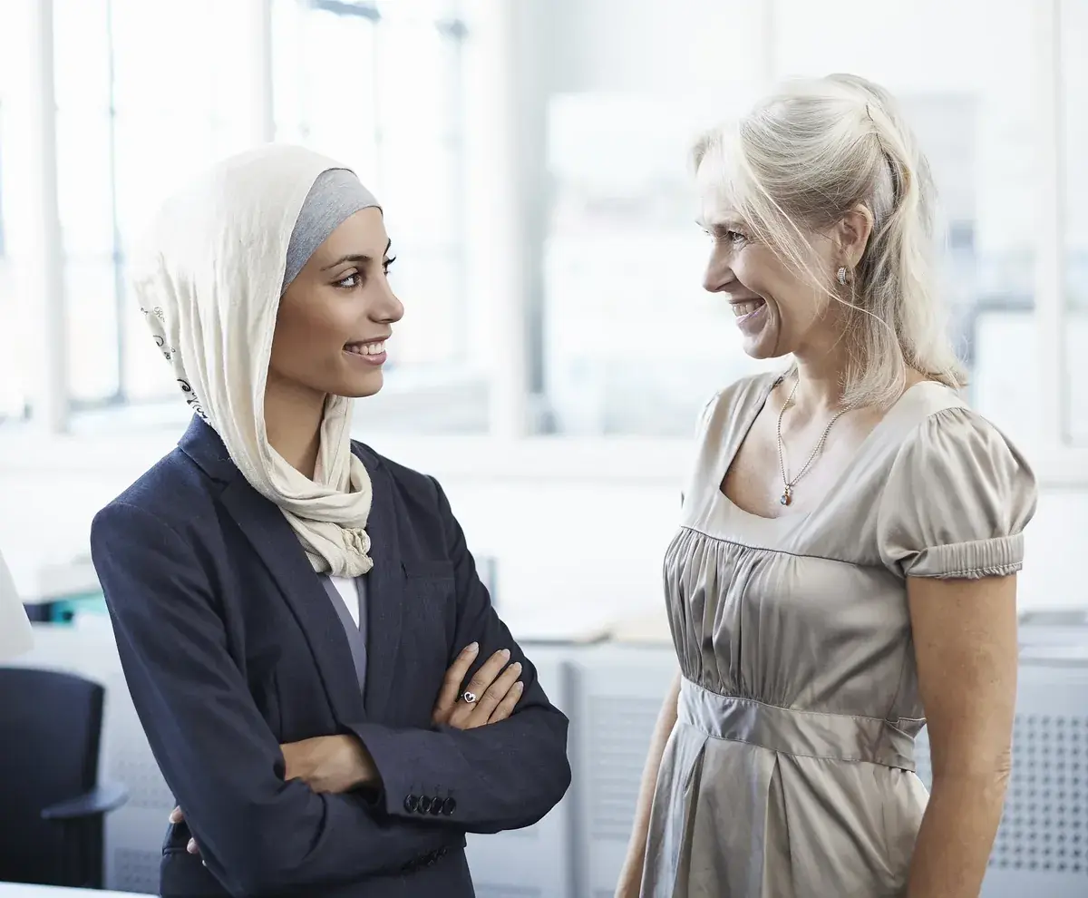 Twee collega’s staan lachend met elkaar in gesprek in een licht kantoor