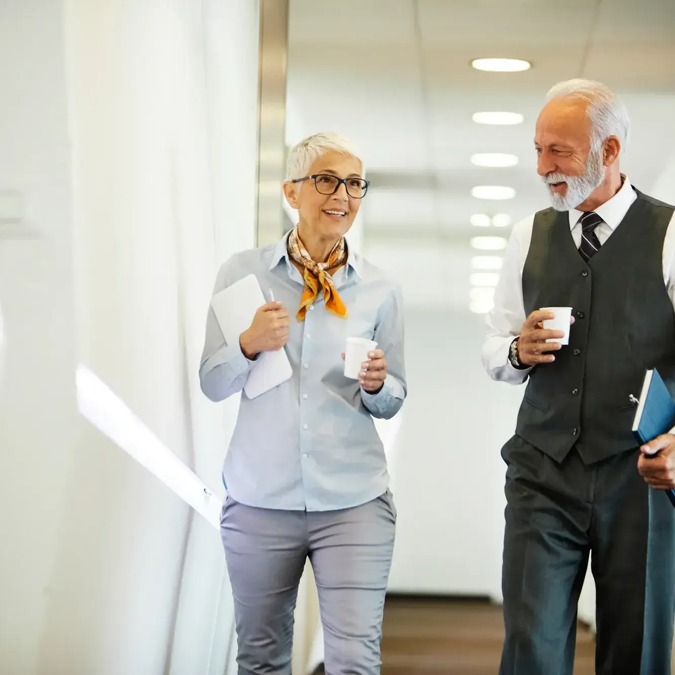 Ervaren manager en collega bespreken de voortgang wandelend door de gang