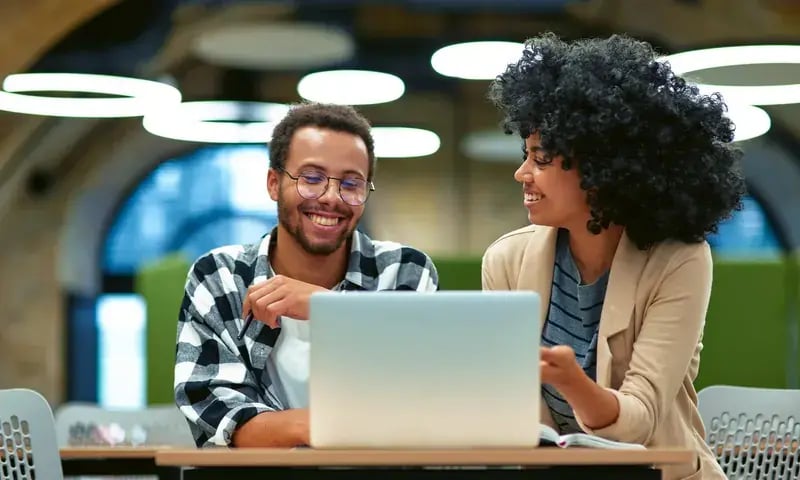 Twee collega’s lachen samen achter een laptop
