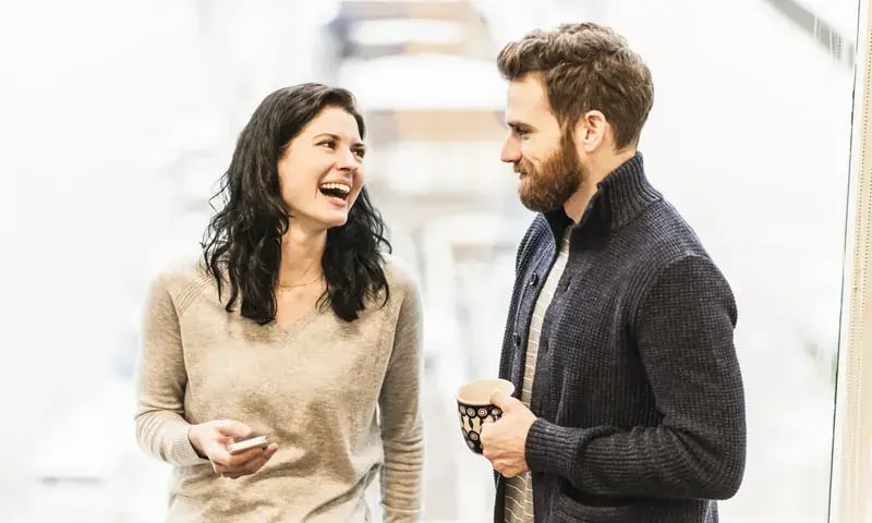 Twee collega’s lachen samen met een kop koffie
