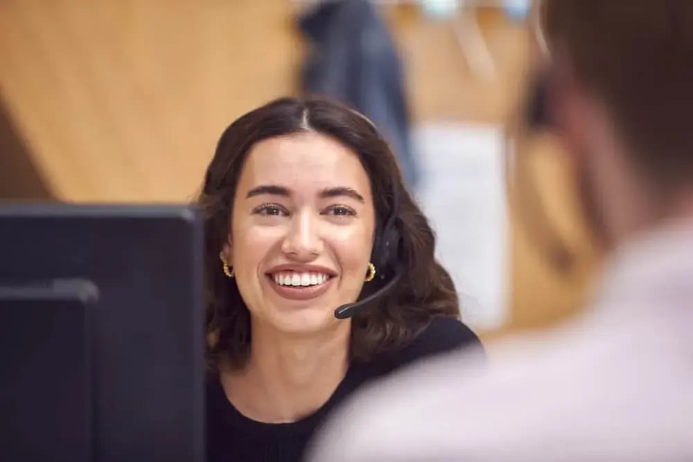 Een medewerker met headset lacht achter haar scherm