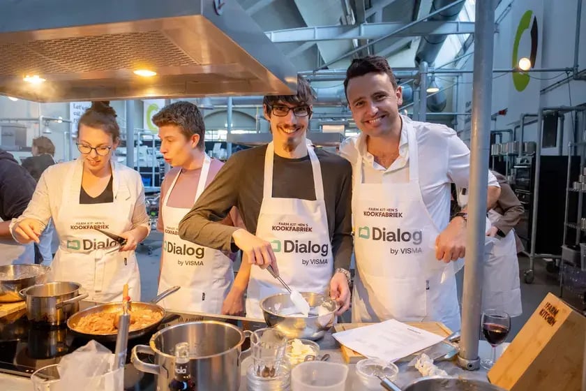 Vier collega’s in Dialog-schorten poseren bij het fornuis
