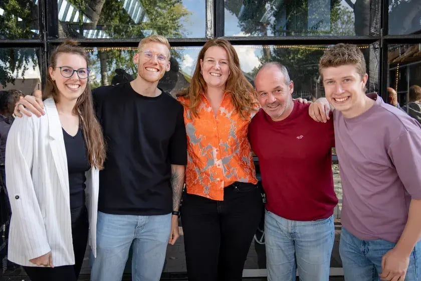 Vijf collega’s arm in arm voor een glazen pui